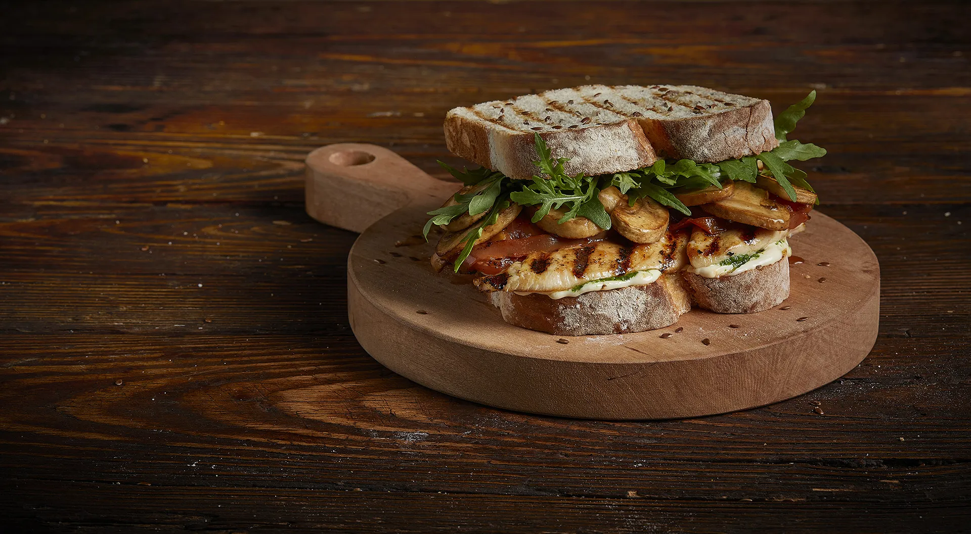 Sándwich de pollo a la parrilla con tomates disecados, champiñones, rúcula y alioli